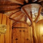 Hébergement Intérieur d’une cabane de Hobbit avec porte, luminaire et tronc de chêne central soutenant un disque en bois sculpté au plafond