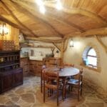 Hébergement Salle à manger d’une cabane de Hobbit avec table, vaisselier et cuisine en arrière-plan à Magné