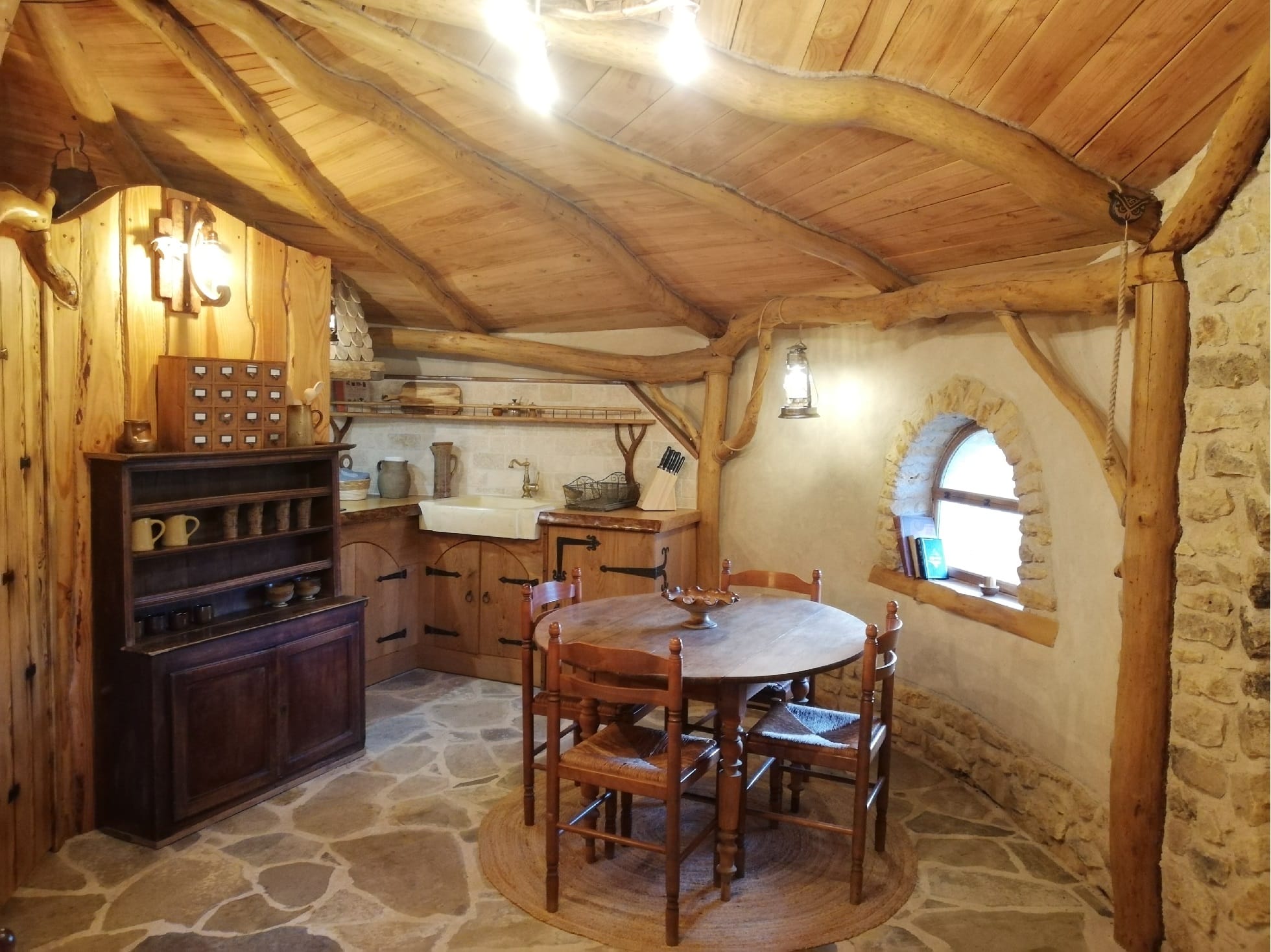 Hébergement Salle à manger d’une cabane de Hobbit avec table, vaisselier et cuisine en arrière-plan à Magné