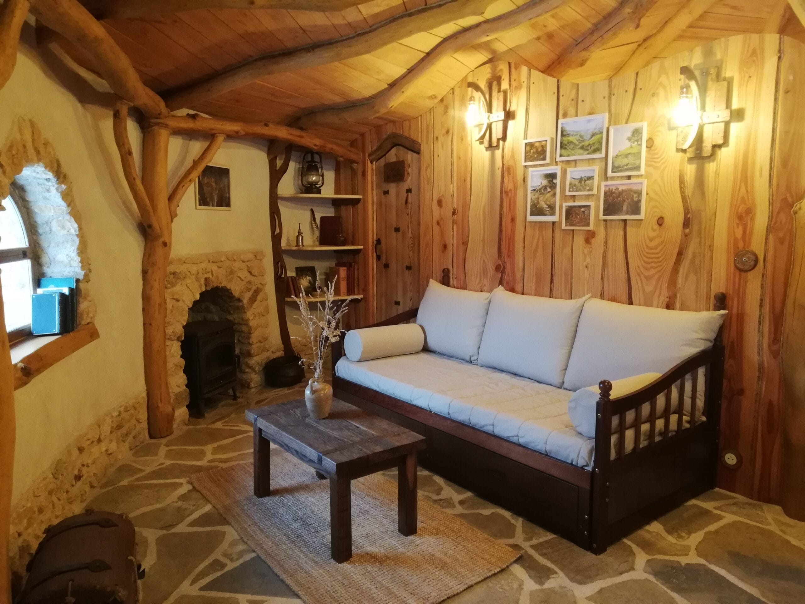 Hébergement Salon chaleureux de la maison de Hobbit du Coteau des Fadets avec canapé, luminaire et fenêtre arrondie à gauche