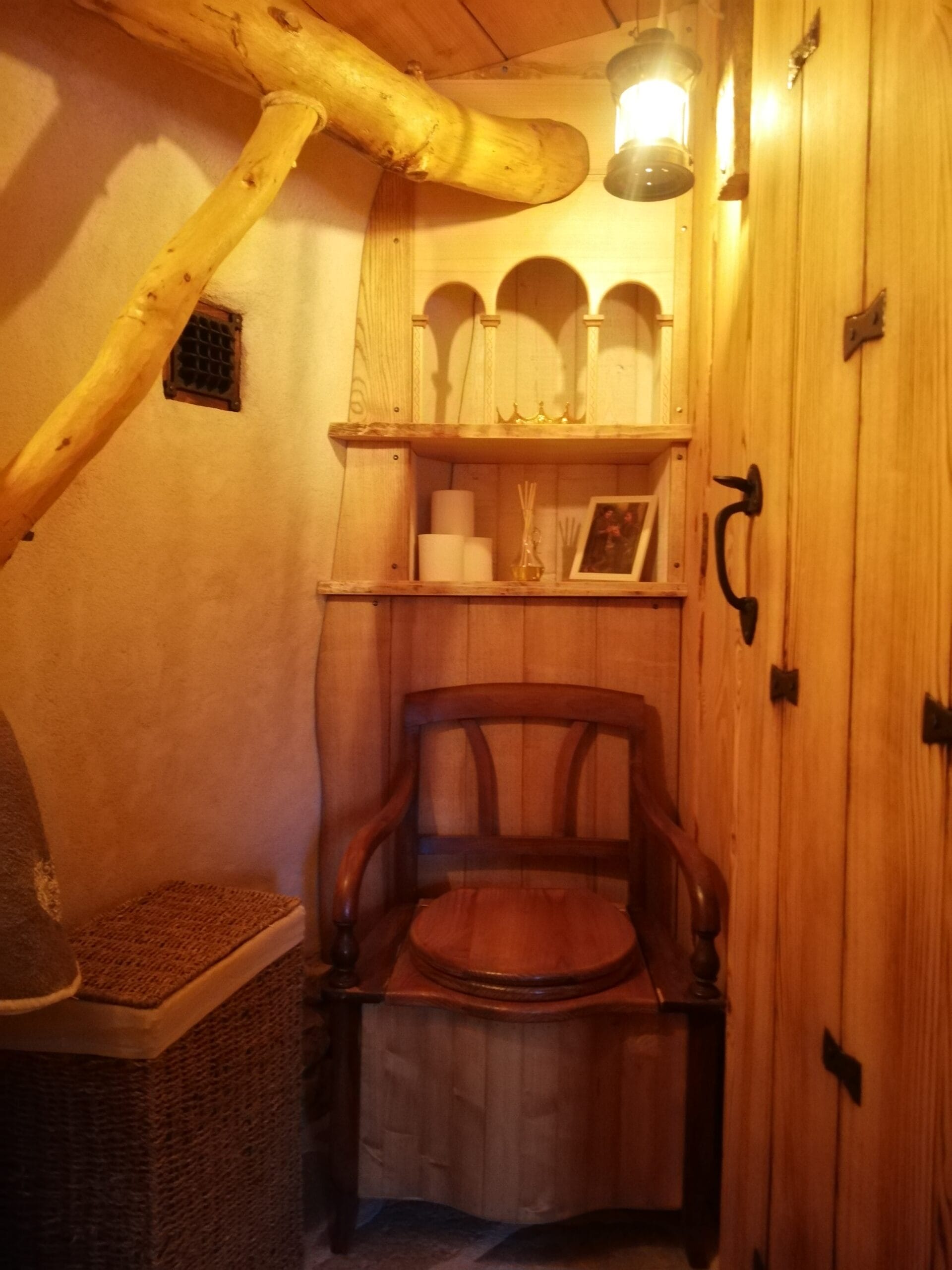 Hébergement Toilette sèche avec ancien siège d’aisance détourné, meuble étagère en bois et luminaire